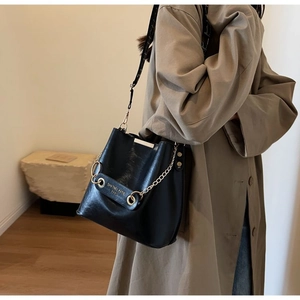 Detailed view of black pebbled leather bucket bag with gold chain and logo branding