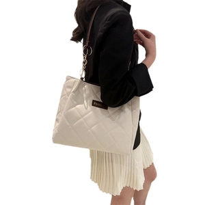 Creamy white quilted tote bag with brown straps and metal chain detail on model