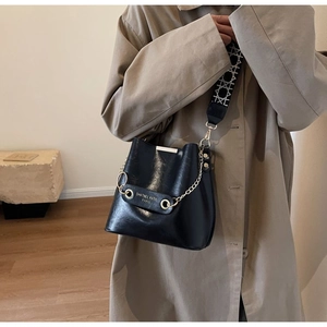 Detail of black bucket bag featuring textured leather and stylish patterned wide strap