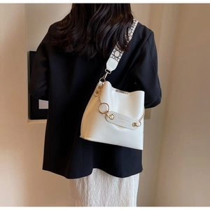 White bucket bag with wide patterned strap and gold chain shown on a model's shoulder