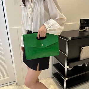 Pochette verde con trama a pietra e chiusura dorata tenuta in un ambiente elegante