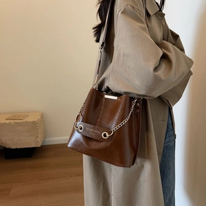 Brown leather bucket bag with gold chain and adjustable strap on khaki trench coat