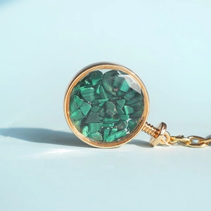 Macro di pendente circolare dorato con cristalli di malachite verde su sfondo blu chiaro