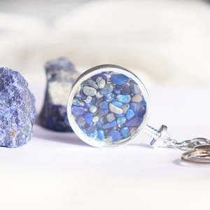 Macro-opname van zilveren sleutelhanger met rond glazen hangertje gevuld met blauwe steen