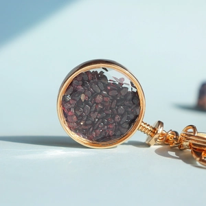 Dettaglio del ciondolo dorato con pietre di granato rosso scuro su sfondo blu