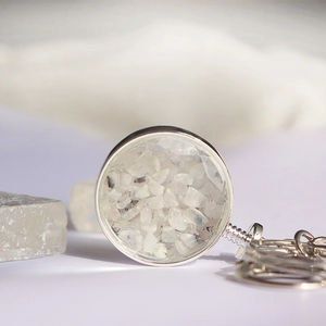 Macro-opname van een ronde zilveren kristallen sleutelhanger gevuld met wit grind