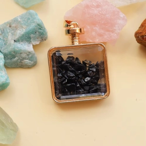 Macro shot of square gold perfume bottle pendant filled with black crystal stones
