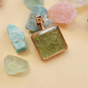 Macro view of gold square perfume bottle pendant filled with green natural crystal stones