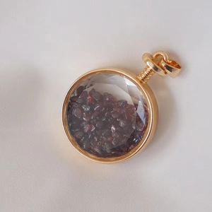 Detailed macro of a round gold perfume pendant filled with dark red crystal gravel stones