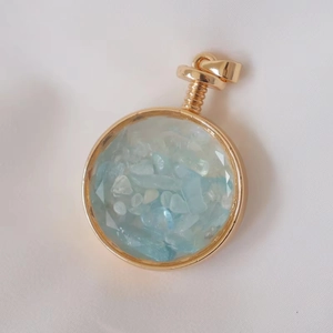 Macro shot of gold-framed round crystal perfume bottle pendant with blue gravel stones