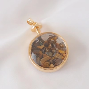 Detailed close-up of a golden round perfume pendant filled with natural tiger eye stones