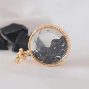 Macro shot of circular gold perfume pendant filled with black crystal stones on fabric