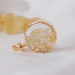 Macro shot of circular gold locket filled with natural citrine stones on white silk