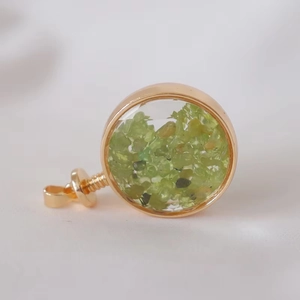Macro shot of gold-framed round crystal pendant with green stone chips on white knit