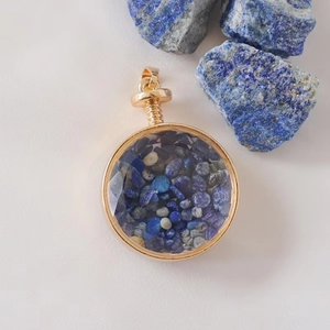 Macro detail of round gold perfume bottle pendant filled with blue crystal gravel stones