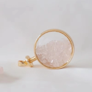 Detail of round gold perfume bottle pendant filled with natural pink crystal stones
