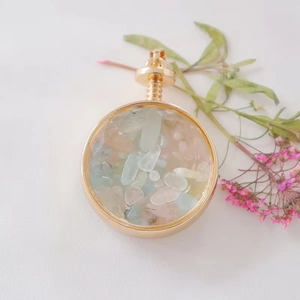 Detail showing round gold perfume pendant filled with colorful crystals and threaded cap