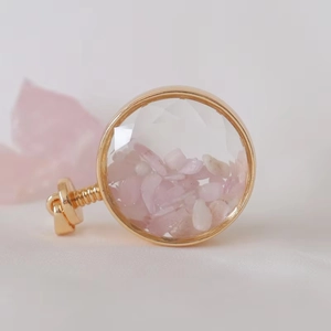 Macro shot of circular faceted glass perfume pendant with pink crystal and gold metal frame