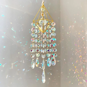 Golden suncatcher with K9 crystals casting rainbow light on a soft gray wall