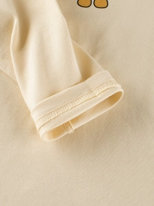 Close-up of cream cotton long sleeve T-shirt cuff with durable stitching and cute cartoon print