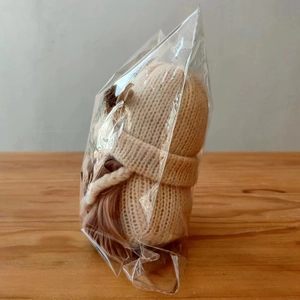 Detail van een beige gebreide dwergpop met fijne geweven textuur in plastic zakje