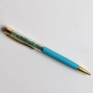 Close-up of a ballpoint pen with turquoise barrel, gold accents and green crystal stones