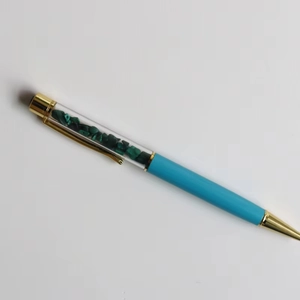 Detail of blue ballpoint pen featuring malachite crystal chips in a transparent barrel