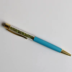 Detail of creative crystal stone ballpoint pen with green peridot and blue metal barrel