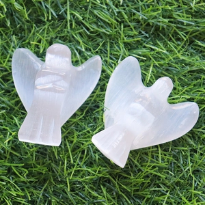 Minimalist carved selenite angel crystal statues on green grass background