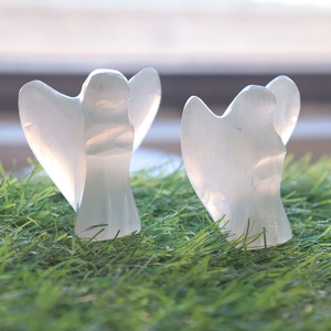 Detail of two translucent selenite angel carvings on green grass with silk-like luster
