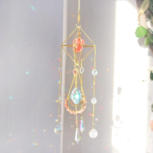 Detail of golden suncatcher with pink crystals and moon shape showing rainbow reflections