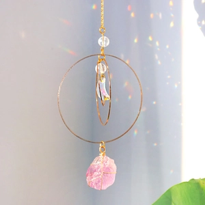 Macro detail of crescent crystal and pink quartz stone hanging from golden rings