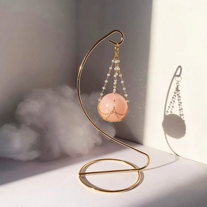 Rose quartz crystal ball pendant with gold metal mesh hanging on a minimalist display stand