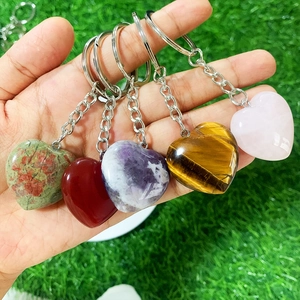 Hand holding five heart-shaped natural crystal keychains over a green grass background