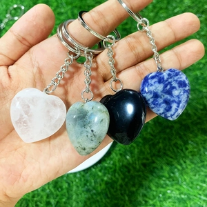 Set of four heart-shaped crystal keychains with various gemstones held over green grass