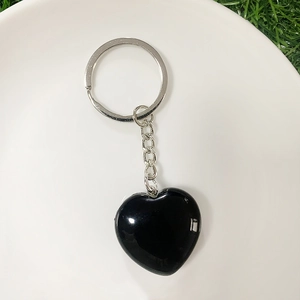 Close-up of a polished black heart crystal keychain on a minimalist white plate