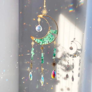 Macro detail of moon-shaped crystal suncatcher with green stones and golden wire wrap