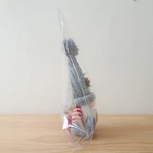 Detail of Christmas gnome plush with grey knitted hat and striped legs in packaging