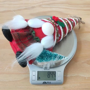 Close-up of a Christmas gnome plush with a red striped hat holding a mini snowy tree