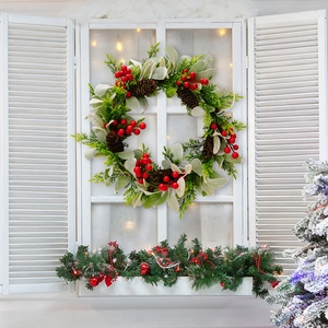 Detailansicht eines Weihnachtskranzes mit roten Beeren und Zapfen am weißen Fenster