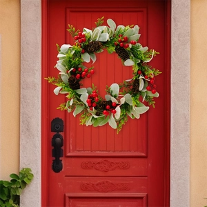 Detailansicht eines Weihnachtskranzes mit roten Beeren und Zapfen an einer roten Tür