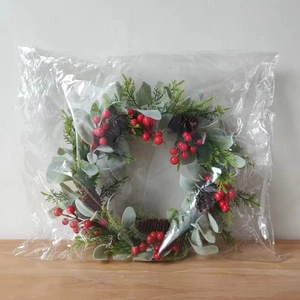 Detail eines Weihnachtskranzes mit roten Beeren und Tannennadeln in Klarsichtverpackung