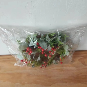 Detail von Weihnachtskranz mit roten Beeren und Tannenzapfen in Klarsichtverpackung