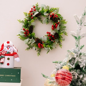 Weihnachtskranz mit roten Beeren, Zapfen und grünem Laub an einer weißen Wand
