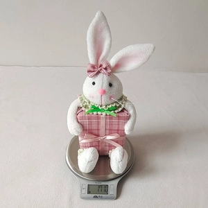 Detailed view of an Easter plush bunny holding a pink checkered gift box on a digital scale