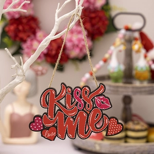 Detail of laser-cut red wooden heart hanger with Kiss Me and love text on white branch