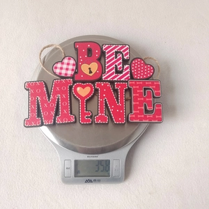Weight measurement of 'BE MINE' red wooden heart pendant showing 35.8g on a digital scale