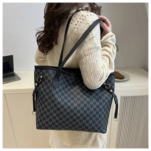 Detail of black tote bag with M-letter print and gold rivets worn by a model in office setting