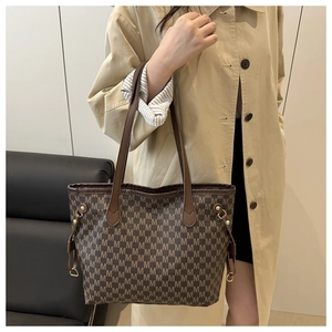Detail of a brown tote bag featuring 'M' letter patterns and golden metallic hardware