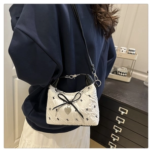 Detailed view of white pleated shoulder bag with black bow and heart pendant on model